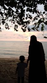 Rear view of silhouette man and woman standing on beach