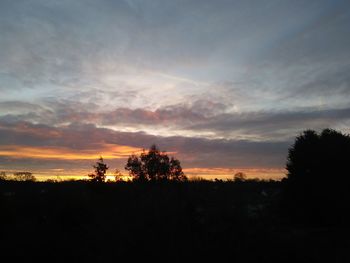 Silhouette trees on landscape against sky at sunset