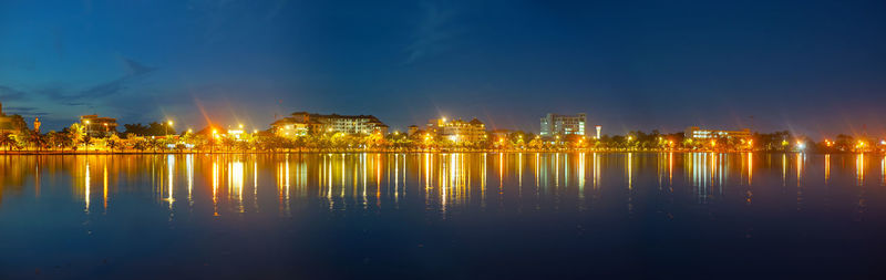 Illuminated buildings by lake against sky in city at night