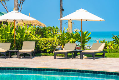 Chairs and tables by swimming pool against sky