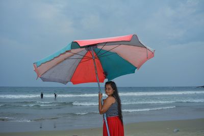 Portrait of smiling woman with parasol standing at beach 