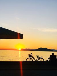 Silhouette bicycle by sea against sky during sunset