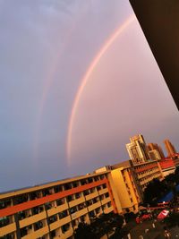 Low angle view of rainbow over buildings against sky
