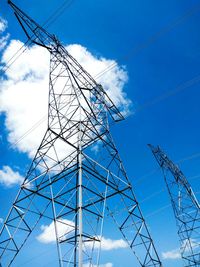 Low angle view of electricity pylon against blue sky