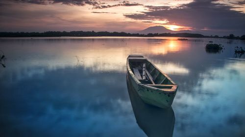 Boat moored on lake against sky during sunset