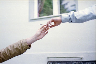 Cropped hand giving cigarette to friend against window