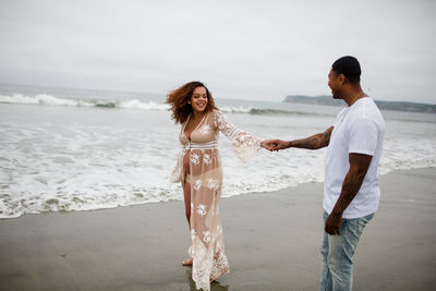 Mixed race couple dancing on beach for maternity photos