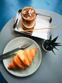 High angle view of croissant in plate and glass of iced latte on table