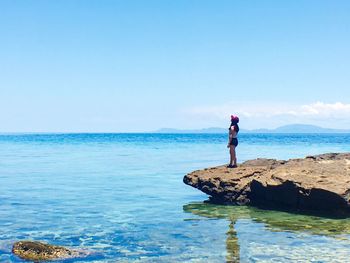 Man standing on rock by sea against clear sky