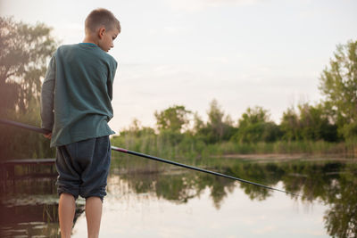 Rear view of boy fishing in lake against sky