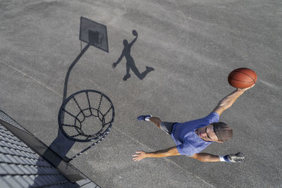 Young man dunking ball in hoop while playing basketball on sunny day