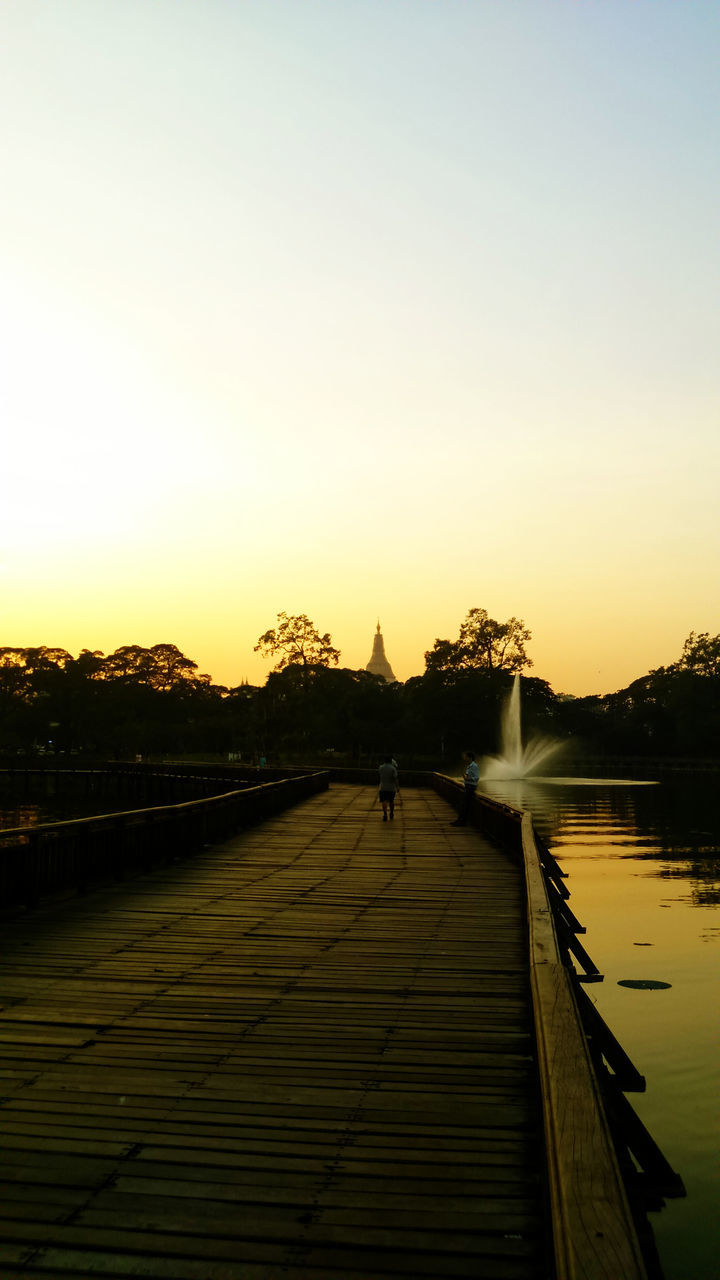 sunset, clear sky, water, the way forward, copy space, built structure, railing, lifestyles, pier, silhouette, architecture, men, orange color, leisure activity, sky, tranquility, nature, river