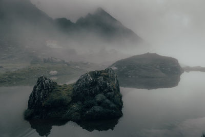 Scenic view of lake by rock formation amidst fog