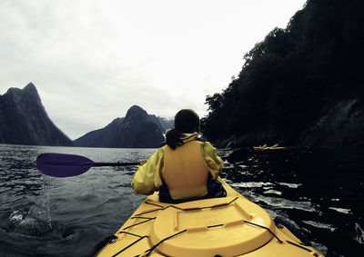 Rear view of woman kayaking over lake against sky