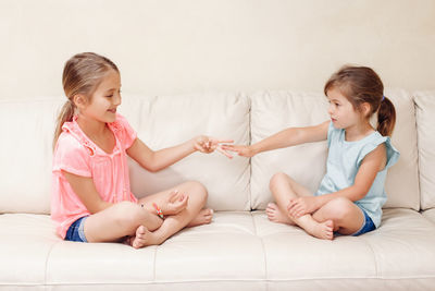 Cute sisters playing while sitting on sofa at home