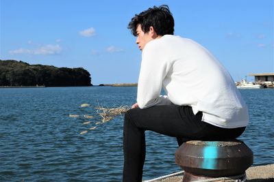 Rear view of man sitting by sea against sky