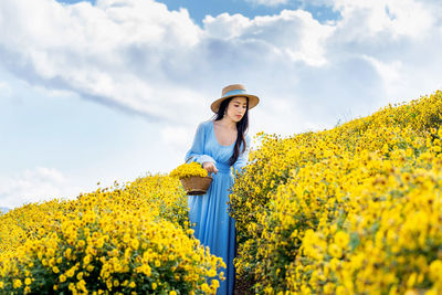 Woman standing by yellow flowering plants against sky