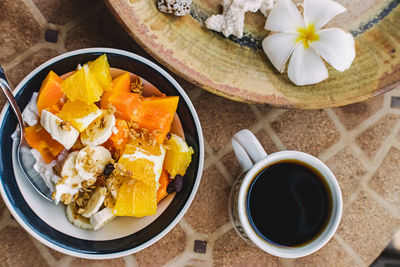 Coffee and breakfast bowl with yogurt and tropic fruits on the stone table, top view