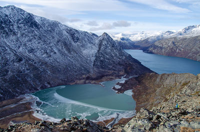 Hiker overlooking turquoise lakes and snowcapped mountains from the top of the knutshøe mountain