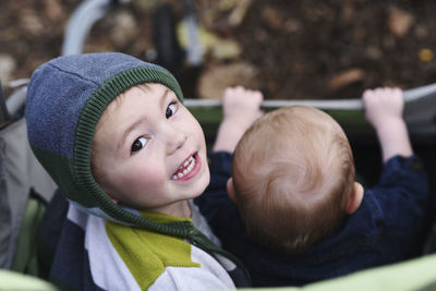 High angle portrait of boy sitting with brother in baby stroller at park