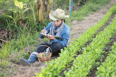 Full length of female farmer writing in notepad while sitting at farm