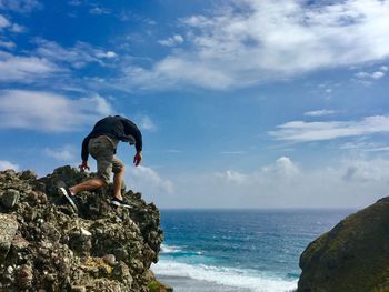 Low angle view of man standing on cliff by sea against sky