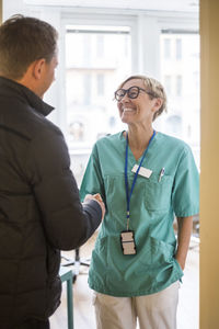 Smiling female doctor shaking hands with mature patient while standing in clinic