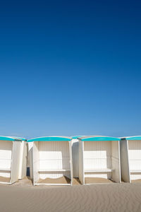 Low angle view of deck chairs on beach against clear blue sky