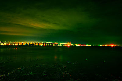 Illuminated bridge over river against sky at night