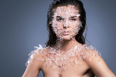 Portrait of woman with broken glass on body against purple background