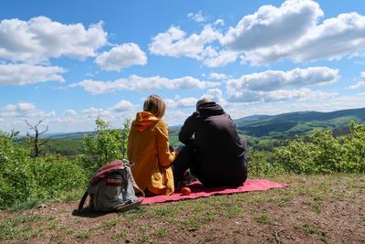 Rear view of women sitting on landscape against sky