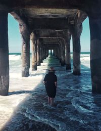 Rear view of mature woman walking under bridge in sea