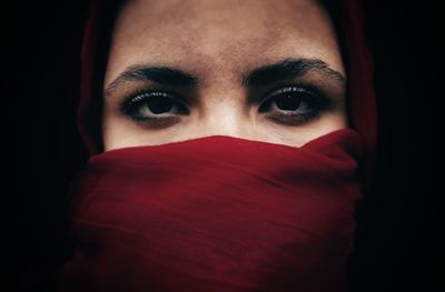 Close-up portrait of woman wearing headscarf against black background