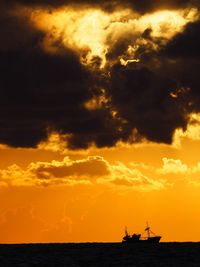 Silhouette ship in sea against dramatic sky during sunset