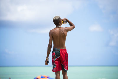 Rear view of shirtless man looking at sea against sky