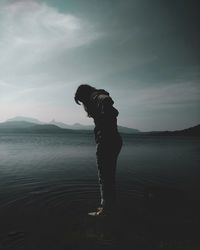 Young woman looking down standing at lake against sky