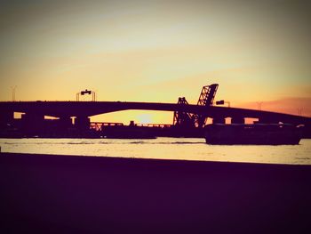 Silhouette bridge over river against sky during sunset