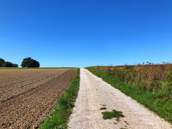 Road amidst field against clear blue sky