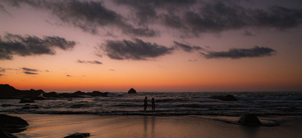 Silhouette people on beach against sky during sunset