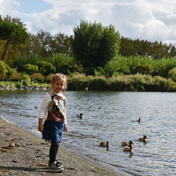 Portrait of girl standing at lakeshore against trees