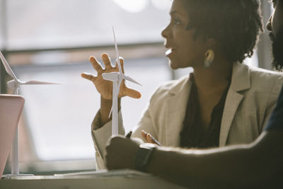 Businesswoman explaining over wind turbine models while sitting with colleague in office