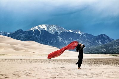 Side view of woman holding scarf standing on land against cloudy sky