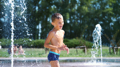 Excited boy of seven years having fun between water jets, in fountain, run around, sprinkle, have