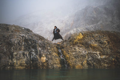 Woman on rock by lake against sky