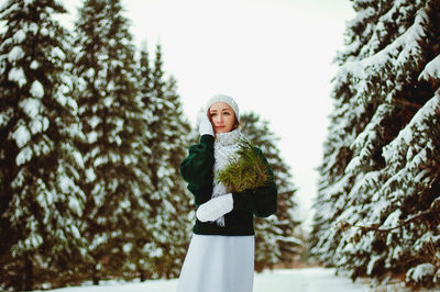 Redhead beautiful woman in green sweater and white gloves walking in the frozen winter forest.