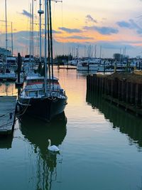 Boats moored in harbor at sunset