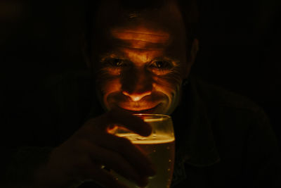 Close-up portrait of smiling man holding alcoholic drink against black background