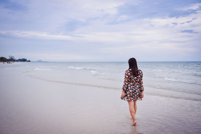 Rear view of woman on beach against sky