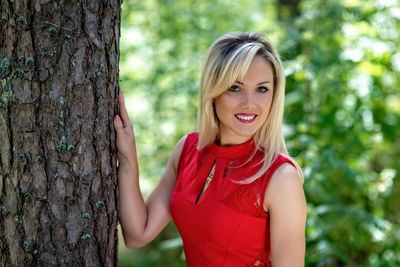 Portrait of smiling young woman by tree trunk