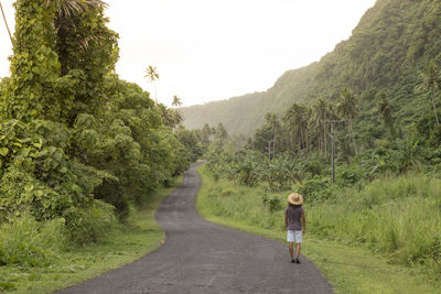 Man with sun hat and curly hair walking on empty road in tropical area